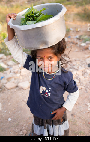 Happy poor lower caste Indian girl standing with a pot of vegetable leaves on her head. Andhra Pradesh, India Stock Photo