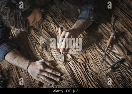 A man working in a reclaimed lumber yard workshop Holding tools and sanding knotted and uneven piece of wood Stock Photo