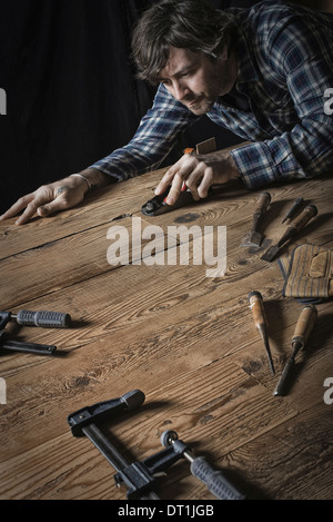 A man working in a reclaimed lumber yard workshop Holding tools and sanding knotted and uneven piece of wood Stock Photo