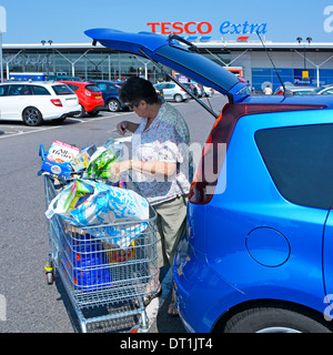 Tesco Extra supermarket store free car park and mature woman loading food shopping into hatchback car Stock Photo