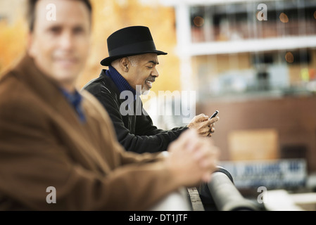 Professional people on the go keeping in contact using mobile phones Two men in coats leaning on a railing Stock Photo