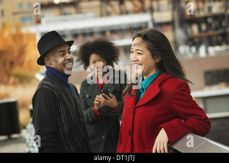 using mobile phones and talking to each other Two women and a man Stock Photo