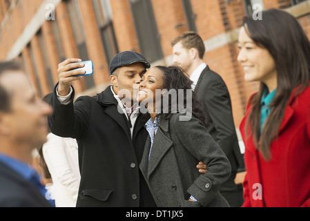 A man holding out a camera phone and taking pictures of the group Kissing a young woman Men and women Stock Photo