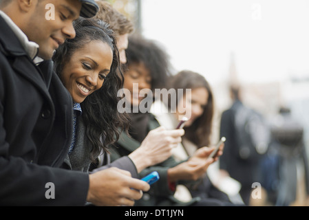 on the go keeping in contact using mobile phones Men and women standing in a line Looking up and laughing Stock Photo