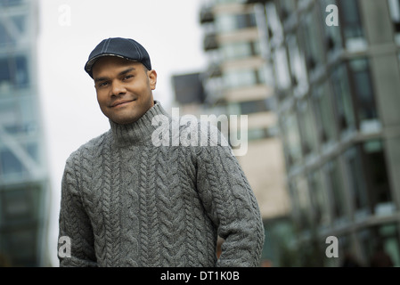 A man in a flat hat and jumper on the street of a city Stock Photo