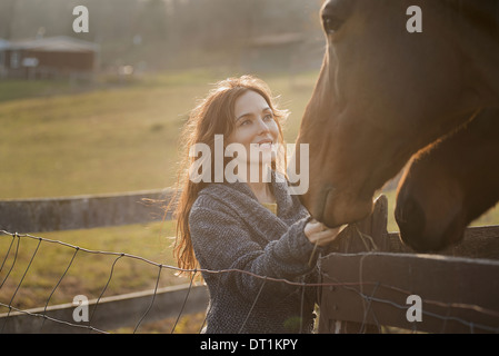 A woman stroking the muzzles of two horses in a paddock on an organic farm Stock Photo