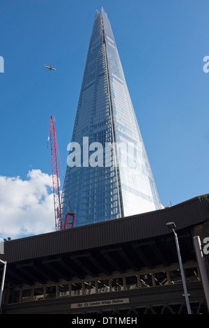 The Shard towering over London Bridge Station with an aeroplane in the blue sky. Stock Photo