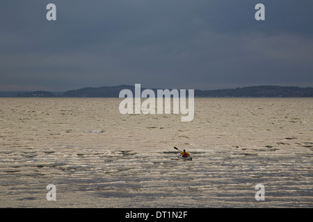 A kayaker paddles his sea kayak in the Puget Sound on a dark and cloudy evening Stock Photo