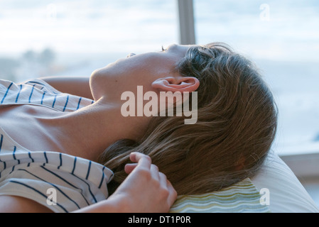 Girl lying on back, looking out window Stock Photo