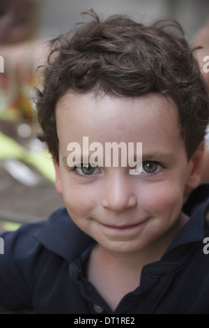 A young boy with dark hair and brown eyes looking upwards and smiling Stock Photo