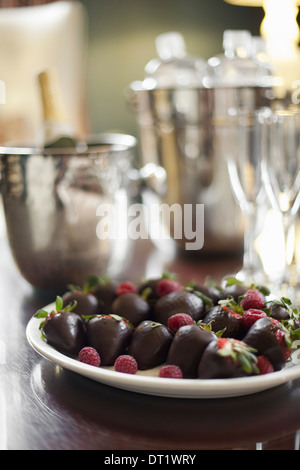 Plate of hand-dipped organic strawberries fruit in artisanal handmade chocolate with raspberry garnish Champagne and glasses Stock Photo