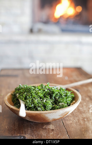 A tabletop with a log fire in the background Green leafy salad in a wooden bowl Stock Photo