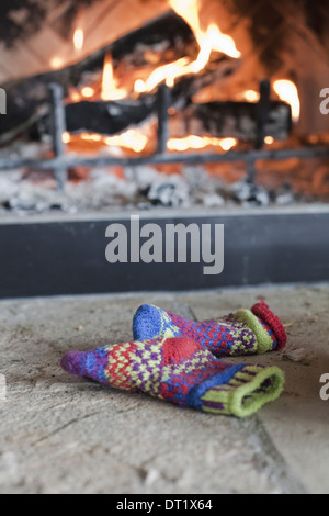 A log fire in a hearth with glowing heart and flames Patterned knitted woollen gloves Stock Photo