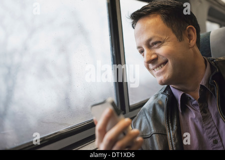 A mature man sitting at a window seat on a train holding his mobile phone Smiling and looking in the distance Stock Photo