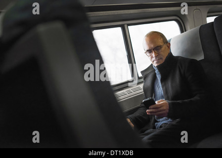 A mature man sitting by a window in a train carriage using his mobile phone keeping in touch on the move Stock Photo