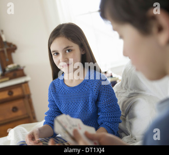 Two children at home sitting side by side and playing a game of cards Stock Photo