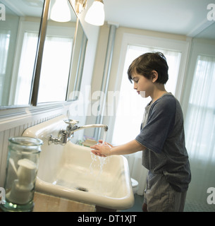 A boy standing in the bathroom washing his hands under the tap Stock Photo