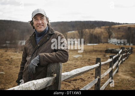 A man leaning against a post and rail fence on a farm in winter Stock Photo