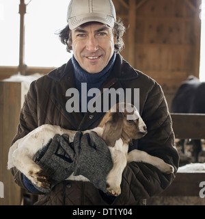 A man holding a small kid goat in his arms in a livestock pen Stock Photo