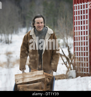 An organic farm in winter in New York State USA A man wheeling a barrow of firewood Stock Photo