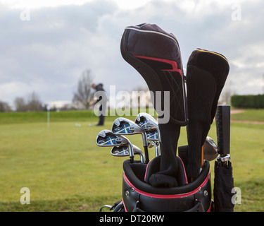 Bag with golf clubs and senior man putting with long putter on putting green at Sunbury Golf Centre, UK Stock Photo