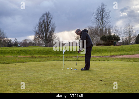 Senior man putts with long putter on putting green at Sunbury golf centre, UK Stock Photo