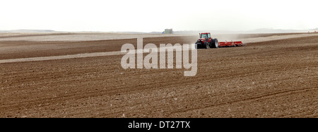 Tractors plowing and planting in a farm field Stock Photo