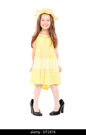 Full length portrait of adorable little girl in fancy yellow dress and hat standing in oversized high heels Stock Photo