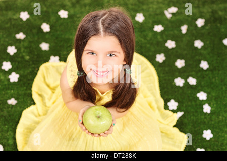 Little girl in fancy yellow dress holding an apple in a meadow full of flowers Stock Photo