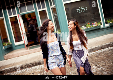 Two teenage girls walking across street, cafe in background Stock Photo