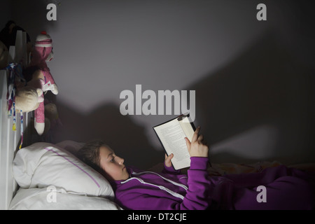 A girl laying in bed reading a book Stock Photo