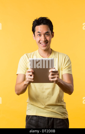 Cheerful Asian man using a tablet PC. In front of Yellow background. Stock Photo