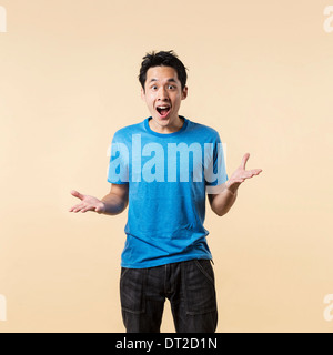 Surprised and amazed looking Asian man standing against cream background. Stock Photo