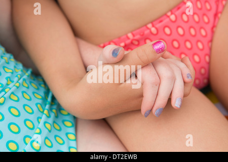 Two girlfriends (6-7, 10-11) sitting on deckchair and holding hands Stock Photo