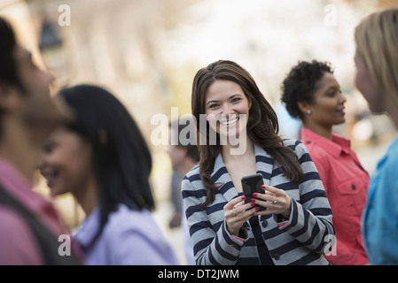 park A young woman holding a mobile phone and looking up at the camera Stock Photo