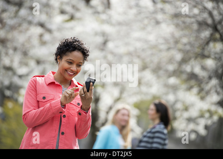 People outdoors in the city in spring time White blossom on the trees A young woman checking her cell phone and laughing Stock Photo