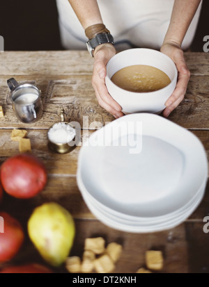 A domestic kitchen tabletop A stack of white plates and fresh pears and a stack of sugar cubes A bowl of fudge sauce Stock Photo