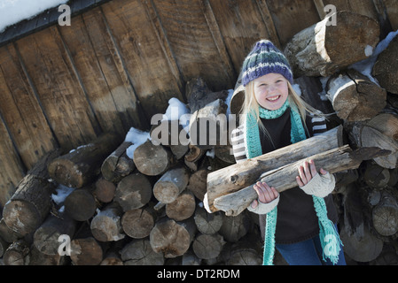 Winter scenery with snow on the ground A girl collecting firewood from the log pile Stock Photo