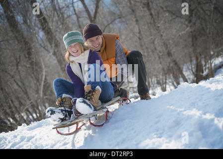 Winter scenery with snow on the ground A man pushing a young woman from the top of a slope on a toboggan