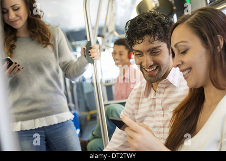 men and women on a city bus in New York city A man wearing headphones and a couple looking at a mobile phone Stock Photo