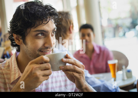 Urban Lifestyle Three young men around a table in a cafe One man taking a drink from a cup of coffee Stock Photo