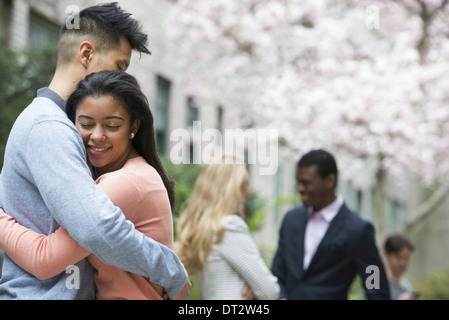 View over cityYoung people outdoors in a city park A couple embracing and two people talking under the trees Stock Photo