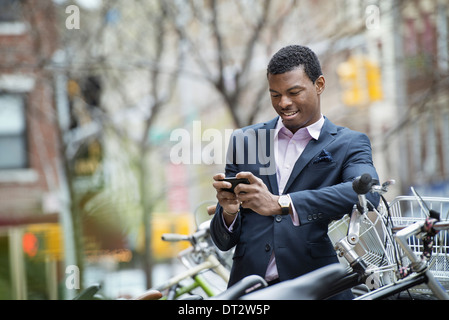 View over cityA young man in a blue suit by a bicycle park Checking his smart phone for messages Stock Photo