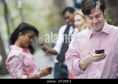 View over cityYoung people outdoors in a city park Three people checking looking down at their cell phones Stock Photo