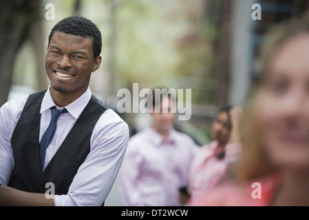 View over cityYoung people outdoors in city park A man with arms folded smiling and three other people grouped around him Stock Photo