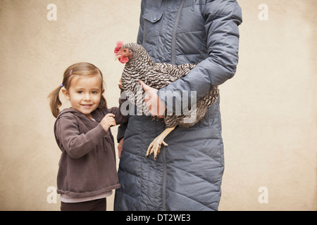 A woman holding a black and white chicken with a red coxcomb under one arm A young girl beside her holding her other hand Stock Photo