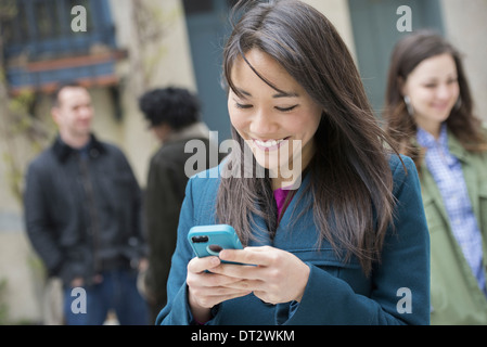 A woman checking her turquoise smart phone among other people on a city street Stock Photo