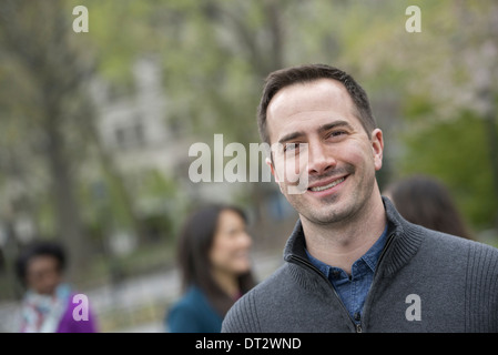 A group of people in a city park A man in a grey sweater smiling Stock Photo