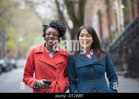 Two women side by side on a city street One holding a cell phone Stock Photo