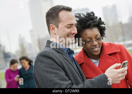 A cityscape view to Manhattan from Brooklyn Four people two in the background and two checking a phone Stock Photo